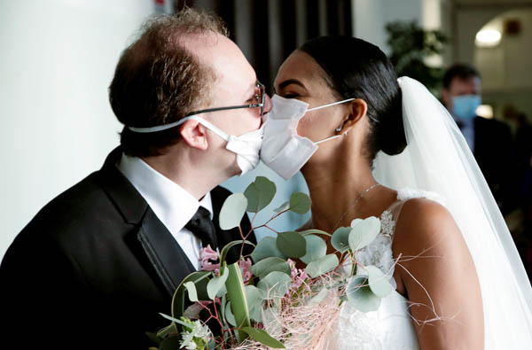 ゲストのいない結婚式で防護マスクを介してキスする新郎新婦