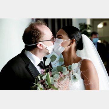 ゲストのいない結婚式で防護マスクを介してキスする新郎新婦