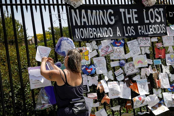 墓地の前で新型コロナに感染し亡くなった犠牲者の名前を記す女性